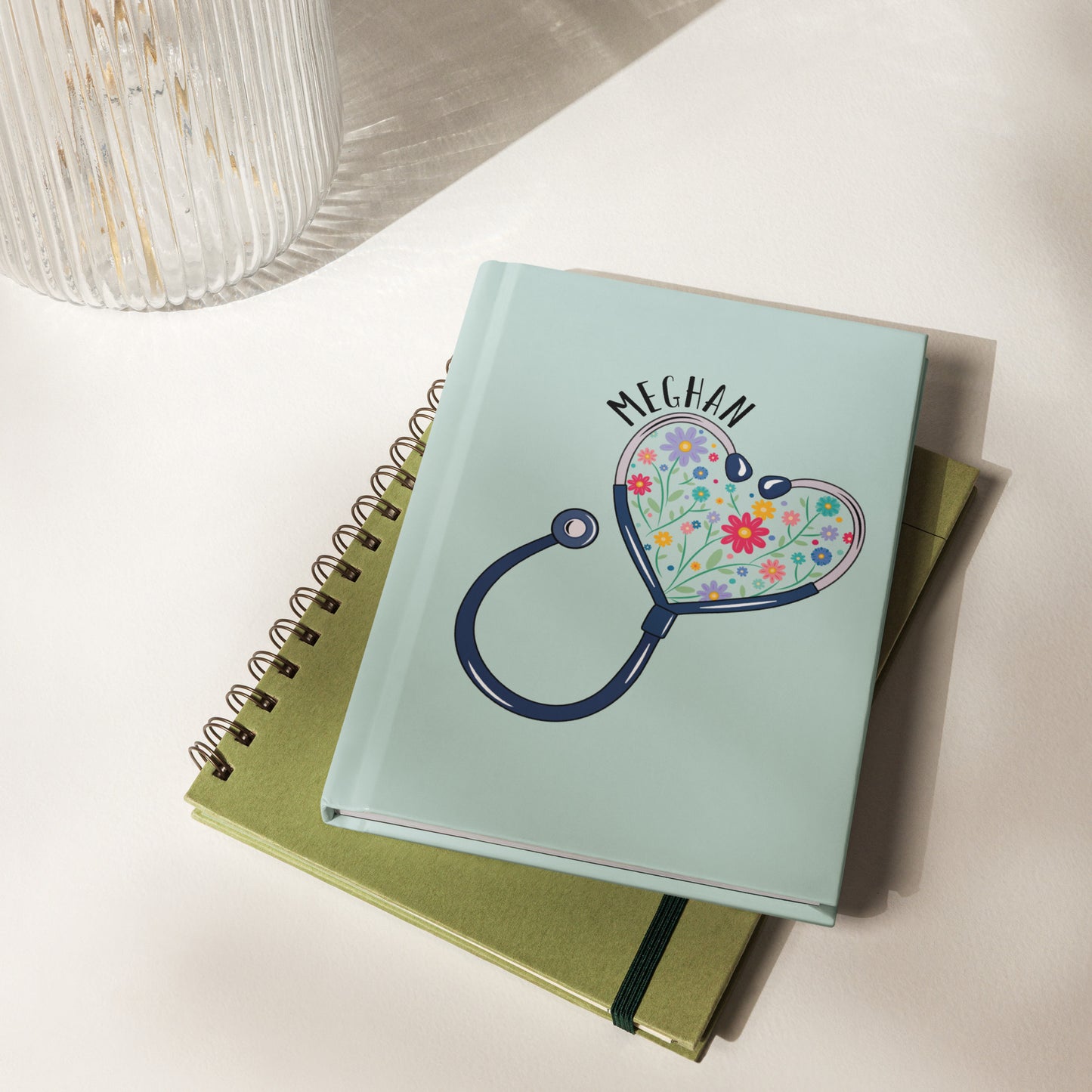Hardcover lined paper journal with a stethoscope in the shape of a heart with multi-colored flowers inside and personalized with a name hugging the top of the heart shape.
